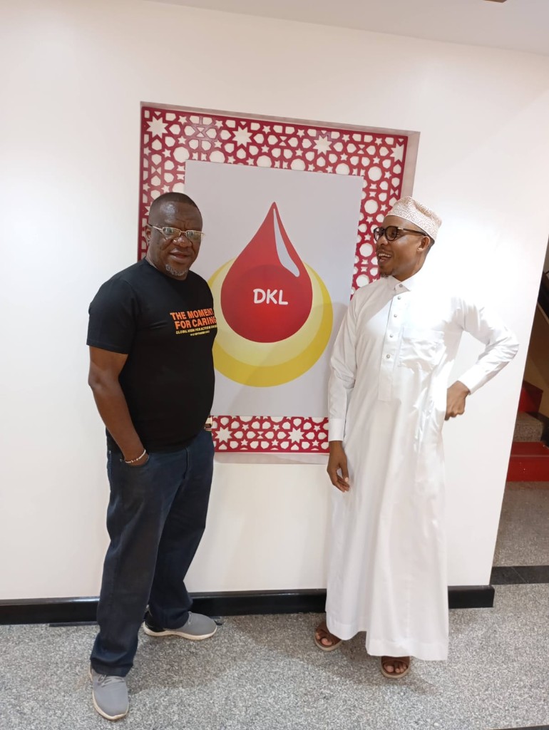 John Gikonyo with a colleague beside a DKL blood-drop poster